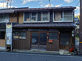 バス停の奥にある木造の2階建ての家屋の写真