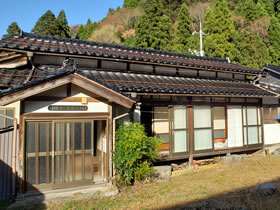 青空と山を背景にした瓦屋根の家屋の写真