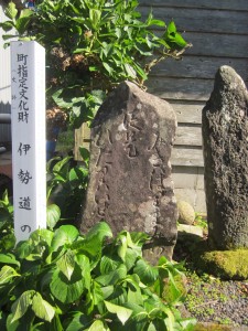 草木のある道沿いにある、伊勢道の道標（新町）の石の建造物の写真