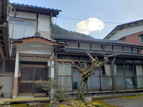 玄関の外に木があり瓦屋根を持つ2階建ての家屋の写真