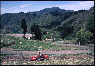 山々を背景に、トラクターが田んぼを田ごしらえしている写真