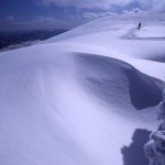雪紋が浮かび上がる雪原を一人の人が歩いている写真