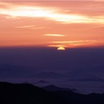 雲の隙間から太陽が3分の1ほど出てご来光している様子の写真