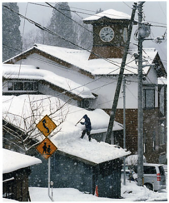 屋根の上に上り降り積もった雪を下ろしている人の写真