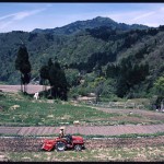 山々を背景に、トラクターが田んぼを田ごしらえしている写真