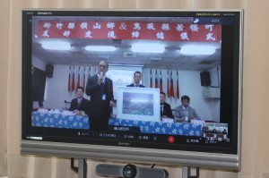 張志弘郷長が記念品を披露しているテレビ中継の写真
