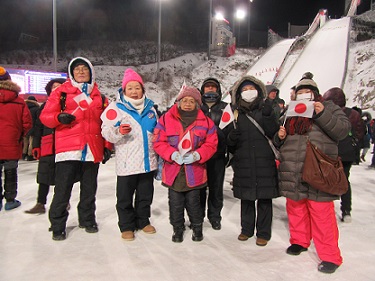 スキージャンプの会場で日本の国旗を持つ6人の集合写真