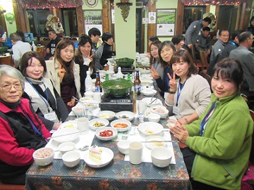 8人がテーブルの周りに座り食事をしながらカメラの方を向いている写真